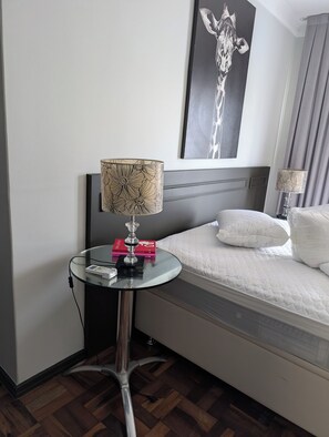 Ein Hotelzimmer mit einem Bett, einem runden Glastisch mit Lampe, einem Wandbild und einer Steckleiste.