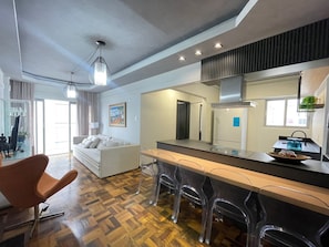 A modern kitchen with a central island, bar stools, and a dining area with a sofa and chairs. - Apartment one block from the beach, central location, close to many attractions. (Balneário Camboriú)