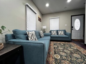 Ein Wohnzimmer mit zwei Sofas, einem gemusterten Teppich und einer Tür mit Fensterteil.