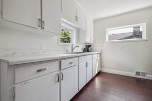 Cocina con armarios blancos, encimera de mármol, ventana y extractor.