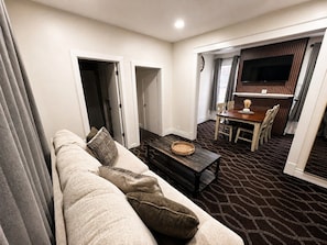A modern living room with a sofa, a coffee table, and a dining area with a TV. - Spacious 5BR Family Home | Near Falls | Parking (Niagara Falls)