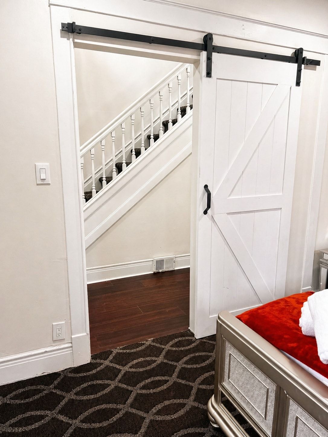 Un dormitorio con una cama, un plaid rojo, una puerta blanca, una escalera y un radiador.