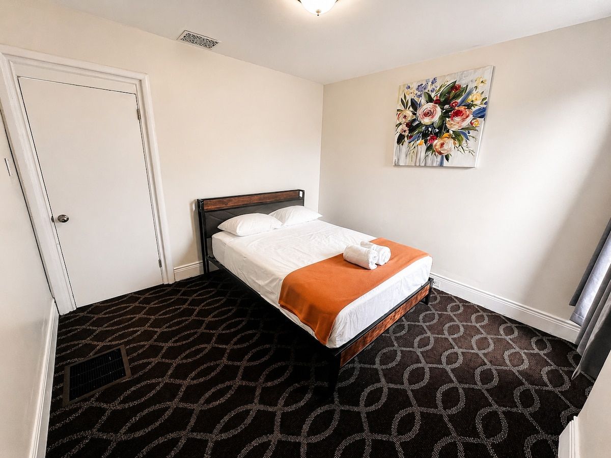 A hotel room with a bed, a door, a radiator, and a painting on the wall.