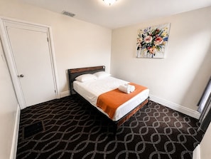 A hotel room with a bed, a door, a radiator, and a painting on the wall. - Spacious 5BR Family Home | Near Falls | Parking (Niagara Falls)