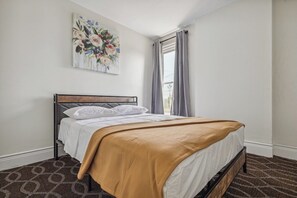 Une chambre à coucher avec un lit, une fenêtre avec des rideaux, un tableau accroché au mur et un tapis à motifs.
