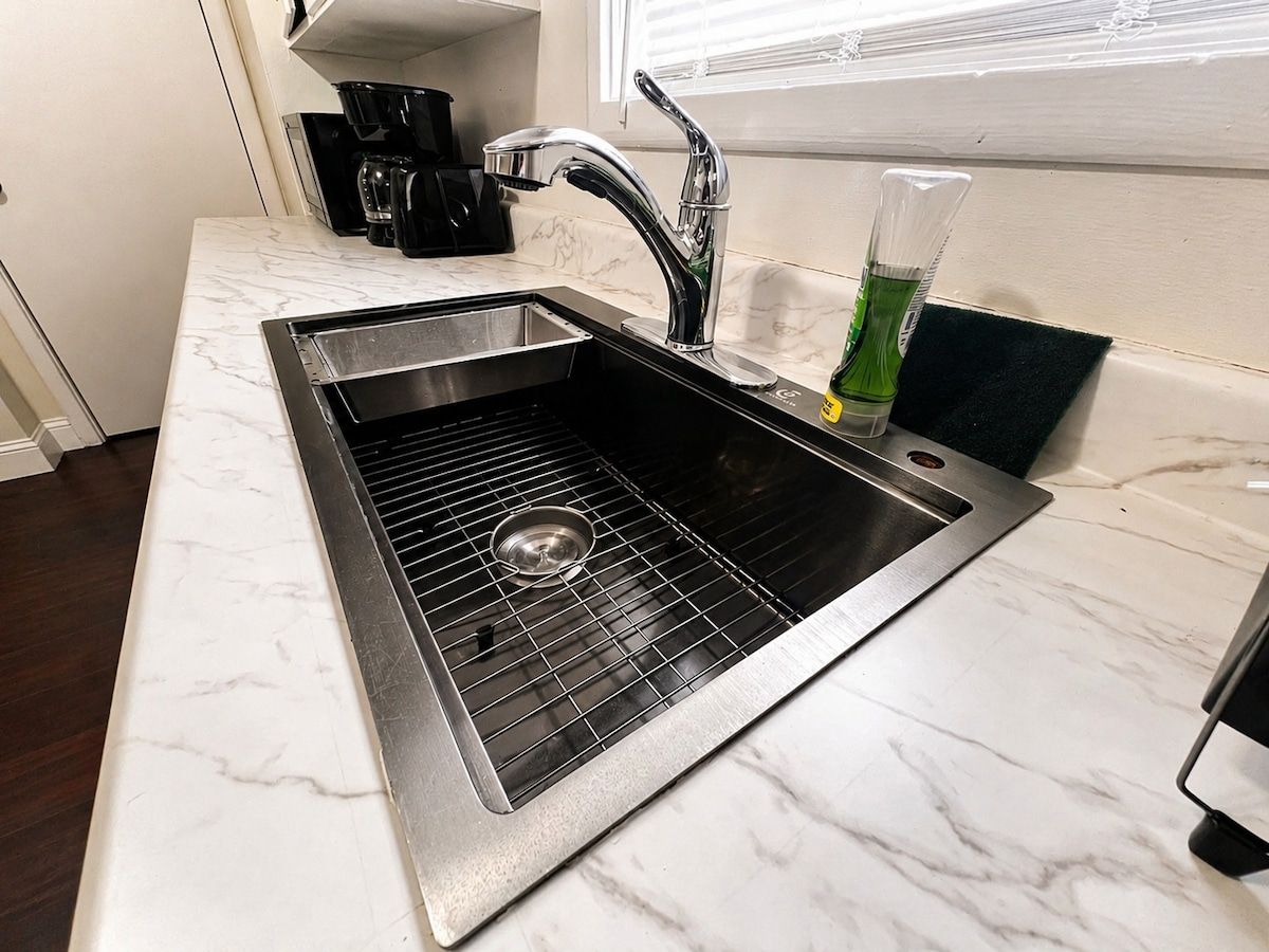 A kitchen with a stainless steel sink, a coffee maker, and a green bottle.