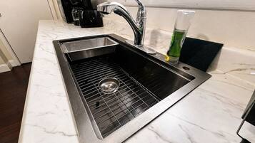A kitchen with a stainless steel sink, a coffee maker, and a green bottle.