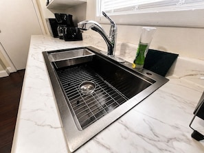 A kitchen with a stainless steel sink, a coffee maker, and a green bottle. - Spacious 5BR Family Home | Near Falls | Parking (Niagara Falls)