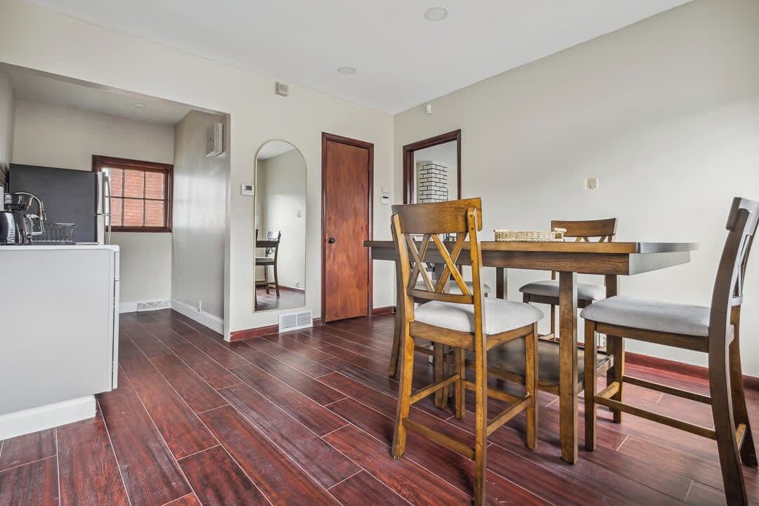 A dining area with a wooden table and chairs, a kitchen with a sink and appliances, and a window with blinds.