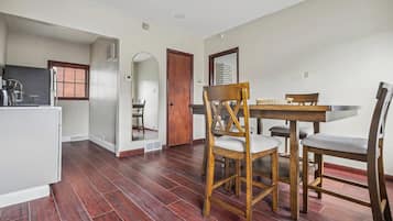 A dining area with a wooden table and chairs, a kitchen with a sink and appliances, and a window with blinds.