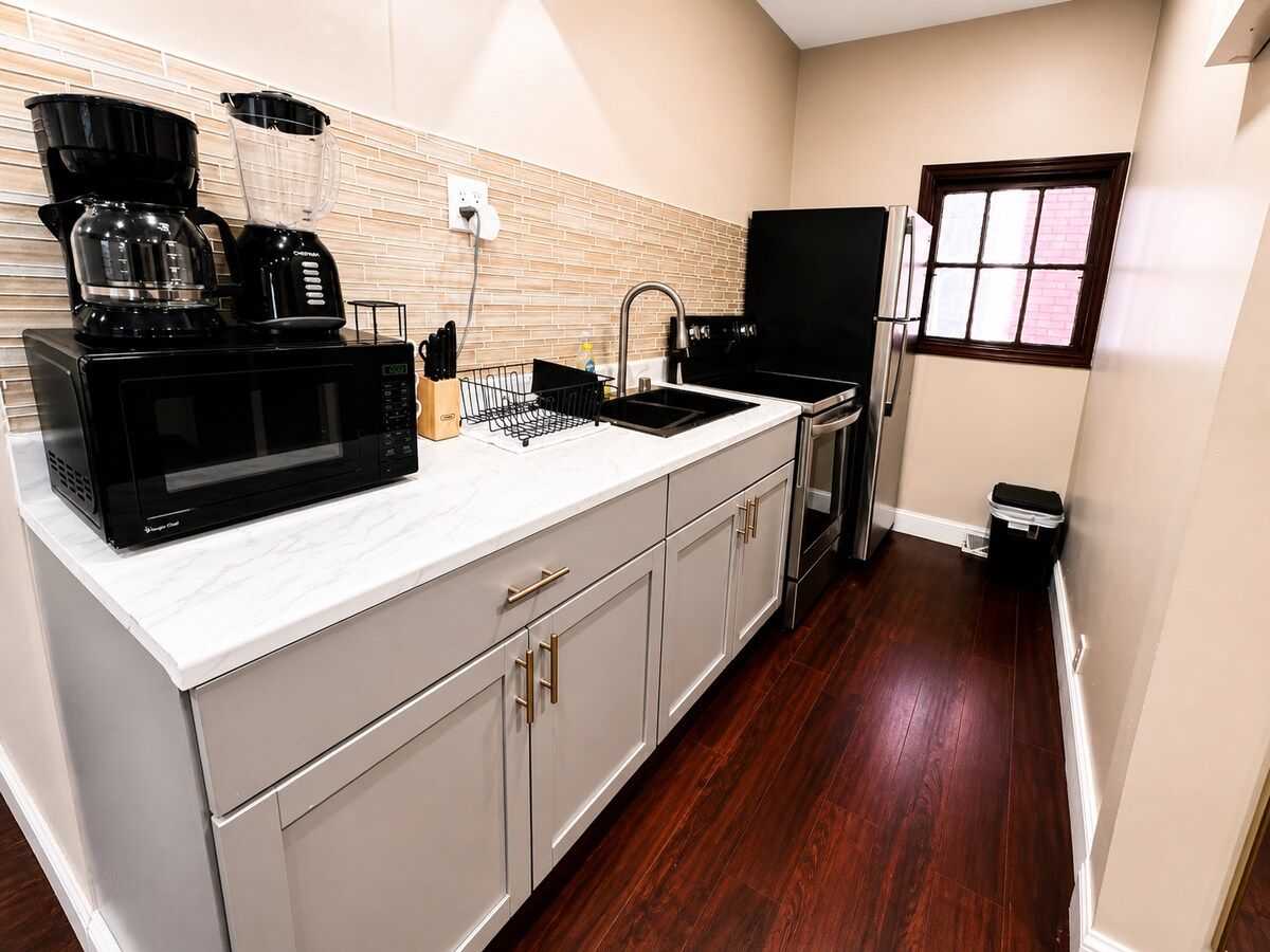 A kitchen with a microwave, coffee maker, and blender on the counter, a sink, and a refrigerator.