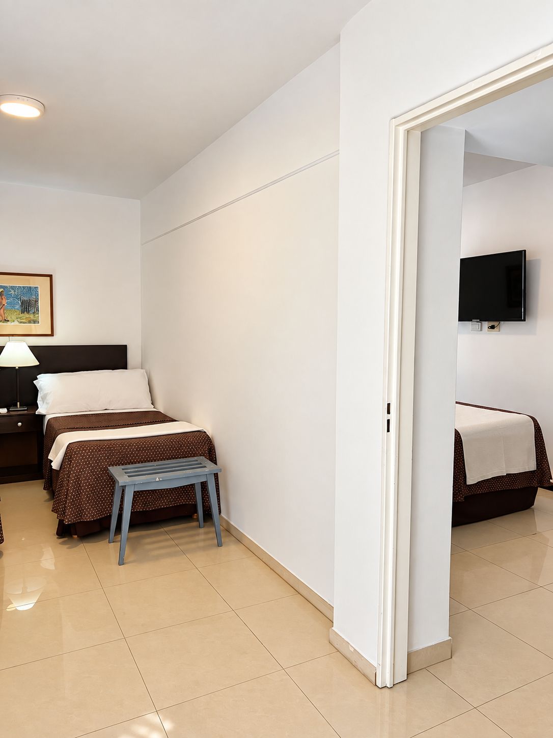 Een hotelkamer met twee bedden, een kleine tafel, een aan de muur bevestigde televisie en een schilderij.