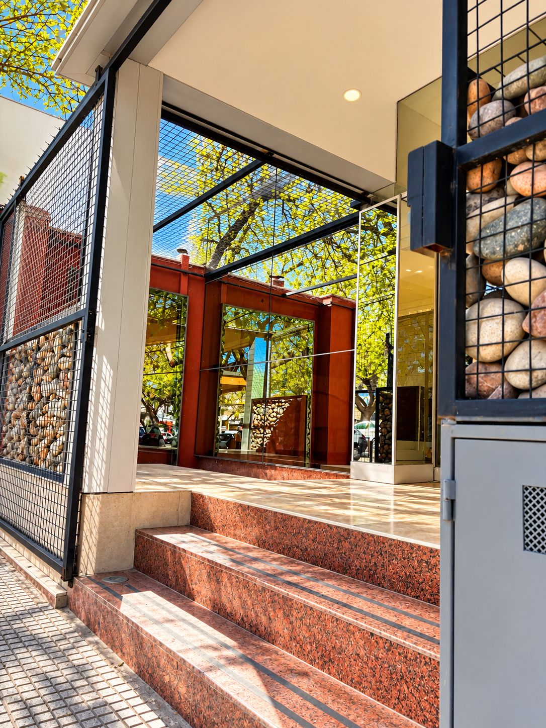 A modern building entrance with a glass facade, a stone wall with pebbles, and a set of steps leading to the entrance.