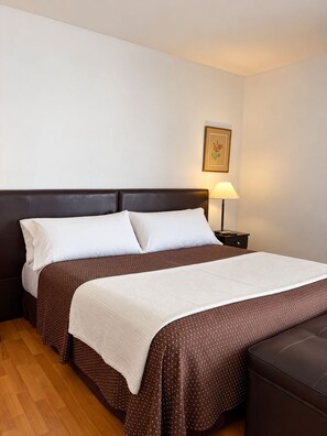 Una cama doble con una colcha marrón estampada y almohadas blancas, una mesita de noche con una lámpara y un cuadro en la pared.