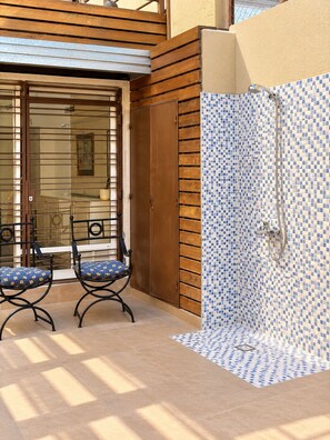 A covered outdoor area with a wooden deck, two chairs, and a shower area with blue and white mosaic tiles. - The Argentina Suites (Mendoza)