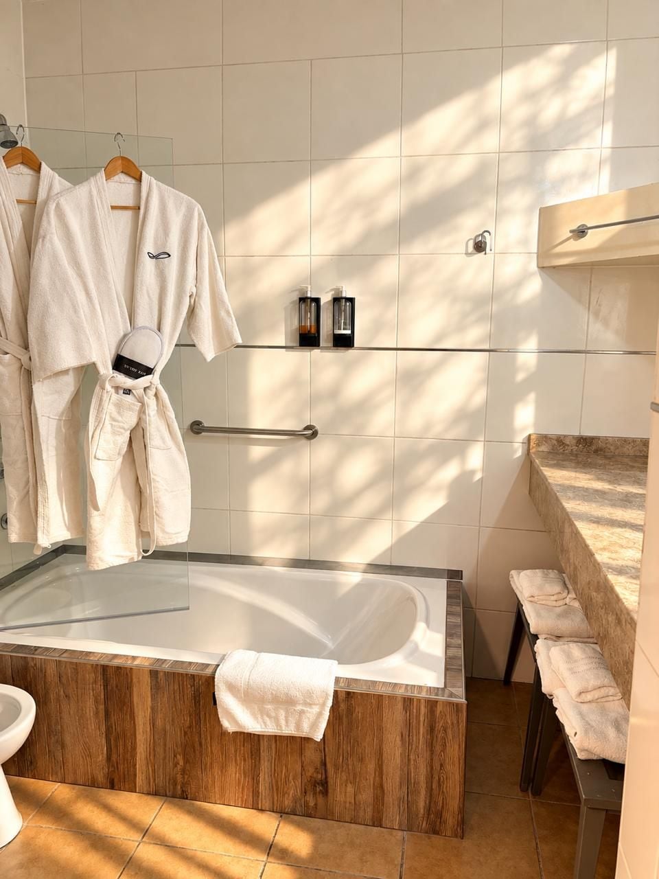 Ein modernes Badezimmer mit einer Glaskabine um ein Bad, einem Holzbadezimmermöbel und einem Handtuchhalter mit Bademänteln.