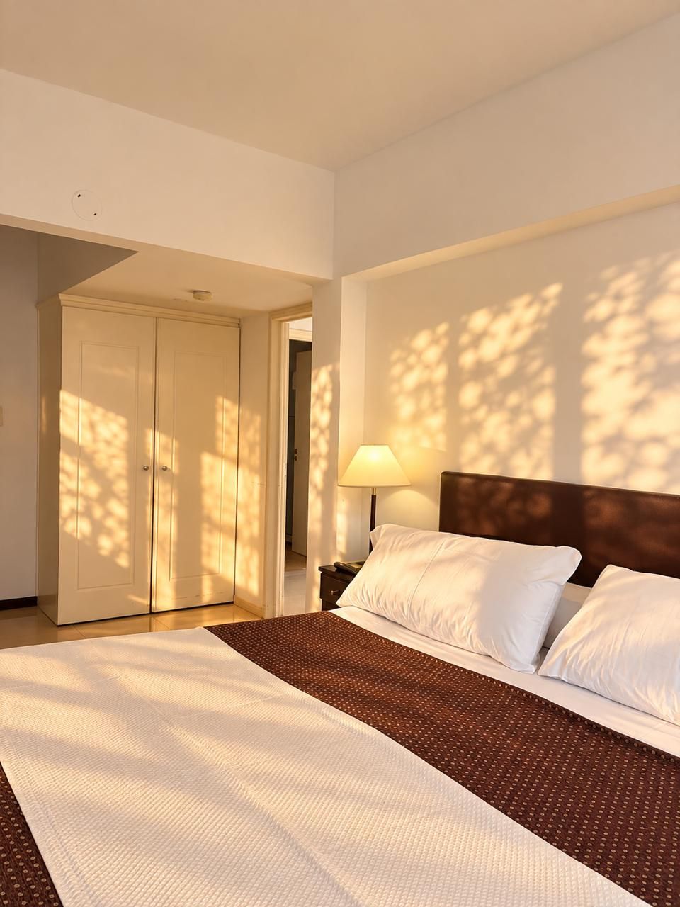 Ein Hotelzimmer mit einem großen Bett, einem Nachttisch, einer Lampe und einem Kleiderschrank.