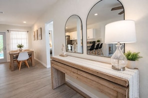 A modern interior with a wooden console table, a large mirror, and a dining area with a table and chairs. - 5BR, Private Pool, Near Pier 60 by Golden Coast Rentals (Clearwater)