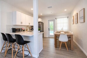 A modern kitchen with white cabinets, a central island with bar stools, and a dining area with a wooden table and chairs. - 5BR, Private Pool, Near Pier 60 by Golden Coast Rentals (Clearwater)