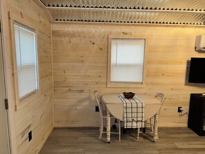 A wooden-paneled room with a table and chairs, a window, and a mounted television. - Quaint Tiny Home with Kitchen (Columbia)