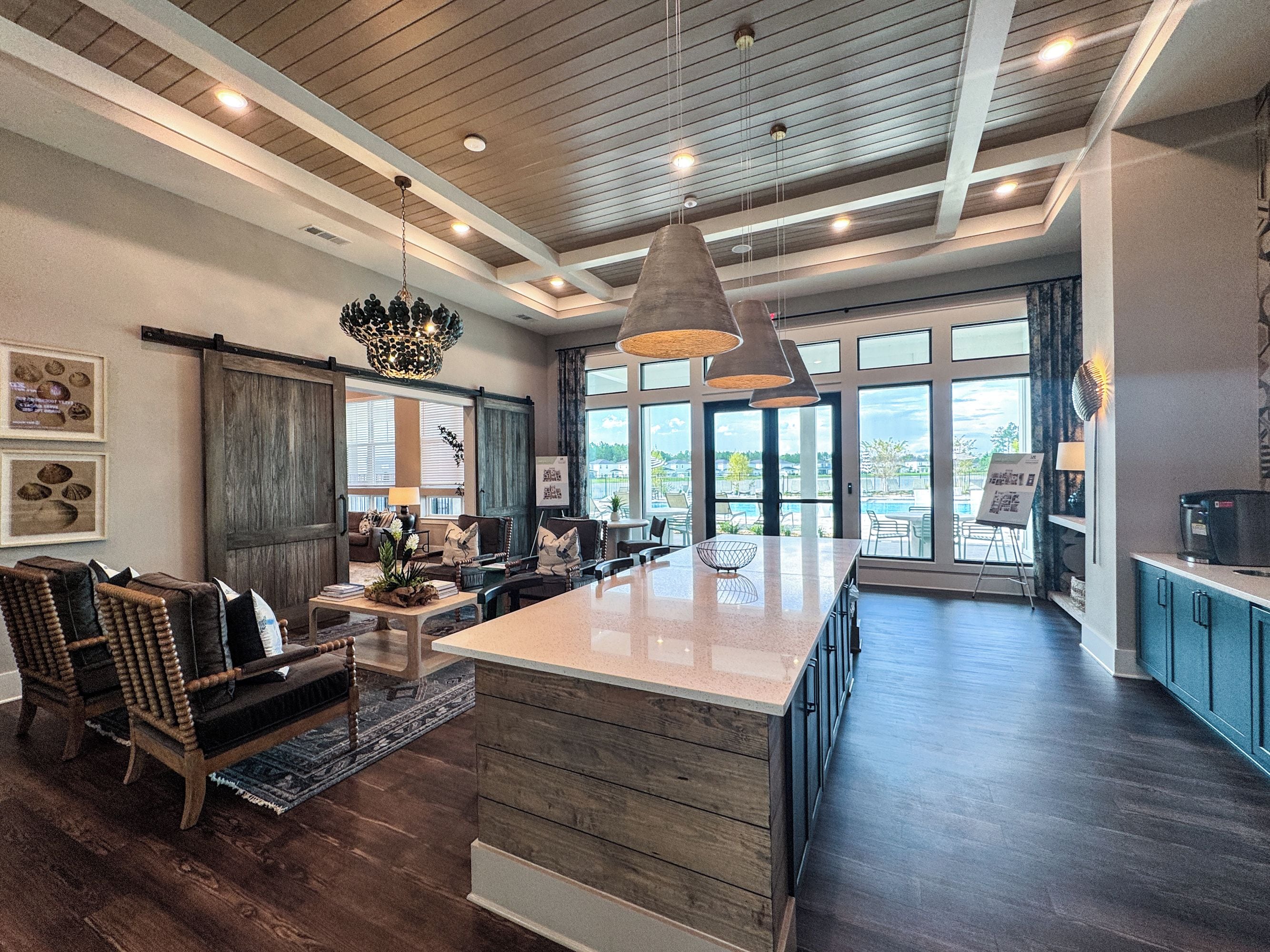 A spacious living area with a large island, dark wood flooring, and a view of the outdoors.