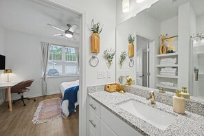 Un baño moderno con encimera de granito, un espejo grande y un ventilador de techo.