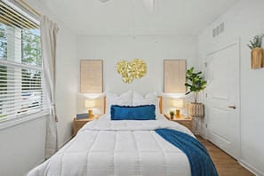 A bedroom with a bed, bedside lamps, a wall art piece, and a potted plant. - Grand Boho Suite / Queen Bed-Pool-Gym Near Airpot (Jacksonville)