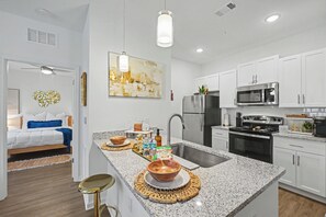 A modern kitchen with white cabinets, stainless steel appliances, and a granite countertop. - Grand Boho Suite / Queen Bed-Pool-Gym Near Airpot (Jacksonville)