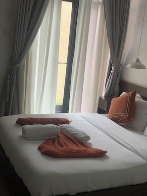 Ett hotellrum med en säng, gardiner, ett nattduksbord och en lampa.