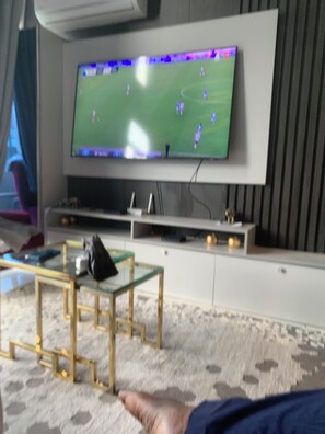 A flat-screen TV mounted on a wall with a remote control on a stand below it. - Charming apartment in beautiful Accra with cool AC and gym access (Accra)