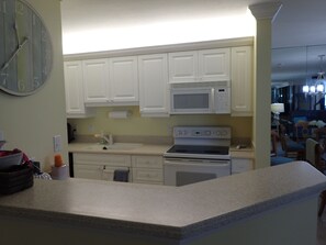 A kitchen with white cabinets, a microwave, an oven, and a clock on the wall. - 2-bedroom beachfront condo in Marco Island with fitness room,pool,picketball (Marco Island)