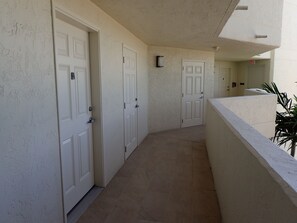 A corridor with white doors, a tiled floor, and a balcony with a railing. - 2-bedroom beachfront condo in Marco Island with fitness room,pool,picketball (Marco Island)