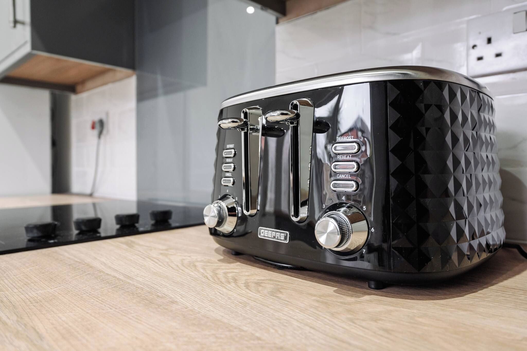 A black toaster with a geometric pattern on the side, placed on a wooden countertop.