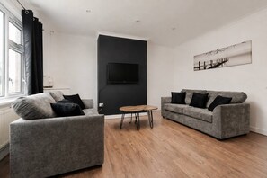 Een moderne woonkamer met twee grijze banken, een salontafel en een flatscreen televisie bevestigd aan een donkere muur.
