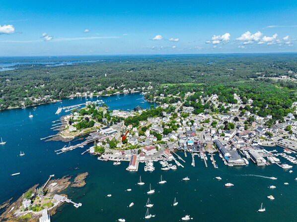 Vue aérienne d’une ville côtière avec un port de plaisance, des bateaux et la végétation environnante.