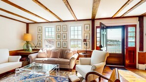 A living room with a sofa, armchairs, a coffee table, and framed botanical prints on the wall. - Rosegate Cottage | Panoramic Harbor Views + Walk Downtown (Boothbay Harbor)