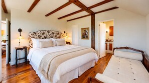 A bedroom with a large bed, bedside lamps, a wooden headboard, and a door leading to a bathroom. - Rosegate Cottage | Panoramic Harbor Views + Walk Downtown (Boothbay Harbor)