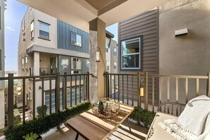 Un balcon avec une table en bois, un panier en osier et une chaise blanche.
