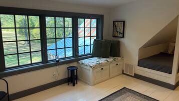 Une pièce avec une grande fenêtre, un banc avec des coussins, un petit tabouret et un lit situé dans un espace en mezzanine.