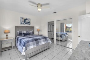 A bedroom with a bed, bedside tables, a ceiling fan, a mirror, and a window with curtains. - Resort‑style 3BR Naples condo w/ tennis, pickle, pool, spa, tiki bar & fitness. (Naples)