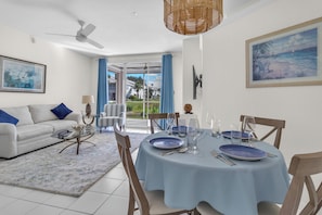 A dining area with a round table set for four, a sofa, and a ceiling fan. - Resort‑style 3BR Naples condo w/ tennis, pickle, pool, spa, tiki bar & fitness. (Naples)