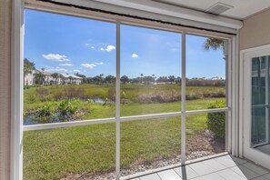 A room with a large window overlooking a grassy area with a pond and trees. - Resort‑style 3BR Naples condo w/ tennis, pickle, pool, spa, tiki bar & fitness. (Naples)