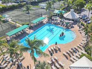 A swimming pool with lounge chairs and umbrellas, surrounded by palm trees and a covered seating area. - Resort‑style 3BR Naples condo w/ tennis, pickle, pool, spa, tiki bar & fitness. (Naples)