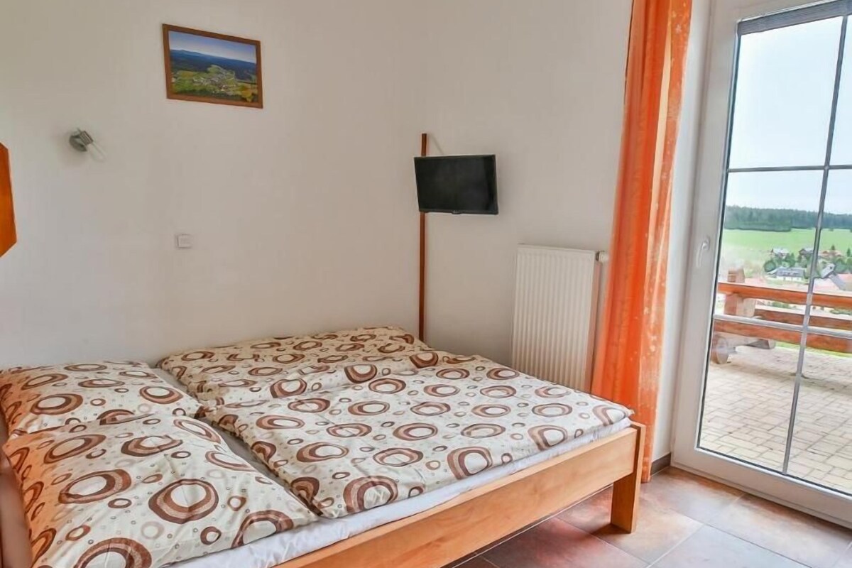 A single bed with patterned bedding, a television mounted on the wall, and a view of the outdoors through a glass door.
