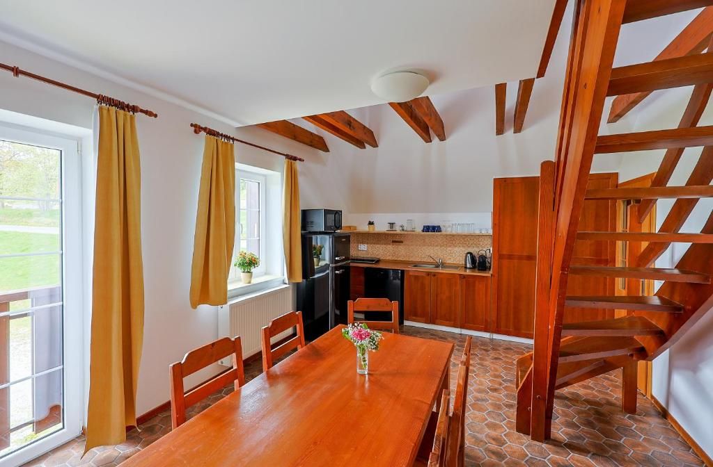 Zona pranzo con tavolo e sedie in legno, una cucina sullo sfondo e una scala in legno.