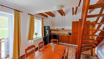 Zona pranzo con tavolo e sedie in legno, una cucina sullo sfondo e una scala in legno.