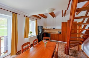 Zona pranzo con tavolo e sedie in legno, una cucina sullo sfondo e una scala in legno.