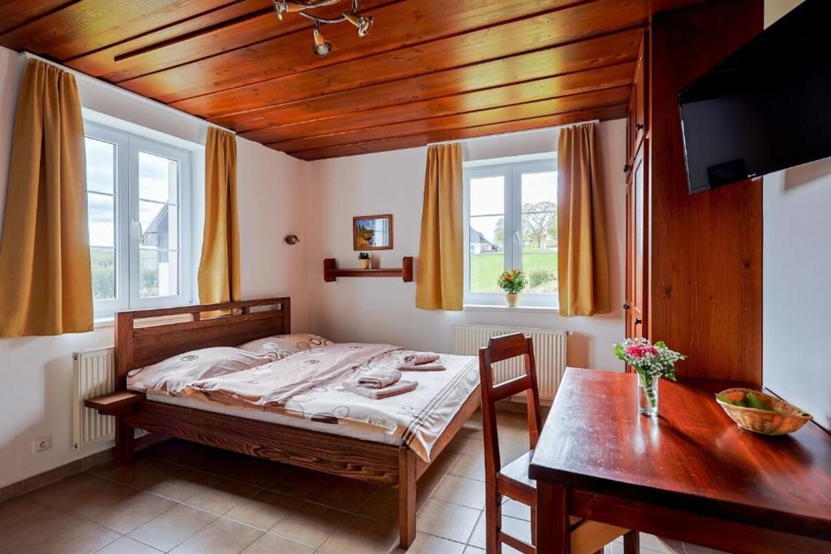 A bedroom with a wooden bed, a wooden table, and a window with curtains.