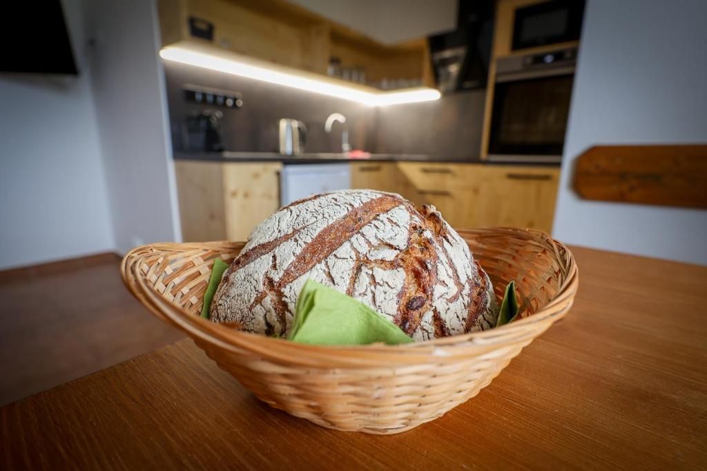 A loaf of bread in a woven basket on a wooden table in a kitchen.