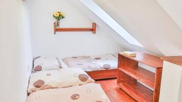 A small, cozy room with a sloped ceiling, a wooden shelf, and a bed with patterned bedding.